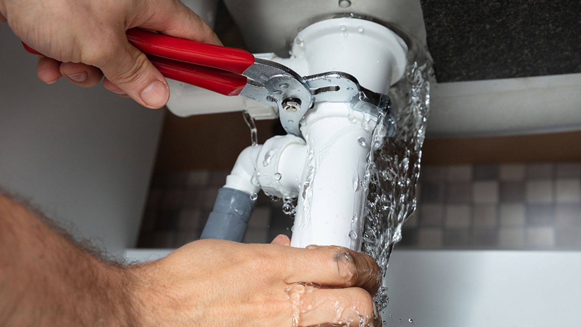Plumber fixing a leaking white pipe with a red wrench